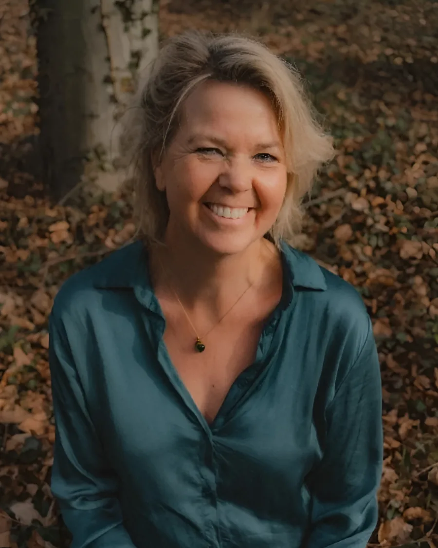 Marjon Ooteman lachend in het bos, zittend tussen de herfstbladeren